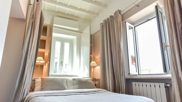 A neatly made bed with a headboard, a window with curtains, and a lamp on a bedside table. - Navona Charming Apartment (Rome)