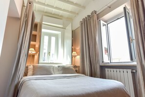 A neatly made bed with a headboard, a window with curtains, and a lamp on a bedside table.
