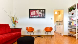 Una sala de estar moderna con un sofá rojo, dos sillones naranja, un reposapiés negro y una obra de arte colgada en la pared.