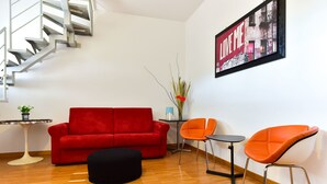 Una sala de estar moderna con un sofá rojo, un reposapiés negro y sillas naranjas. Se ve una escalera al fondo.