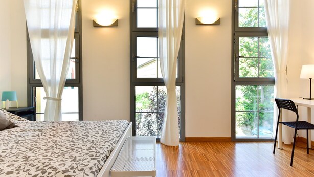 Un dormitorio con cama, escritorio y dos ventanas con cortinas.
