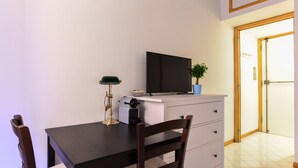 A small, neatly arranged room with a dining table, chairs, a television, a desk with a lamp, and a potted plant. - Spanish Steps Cozy Studio (Rome)