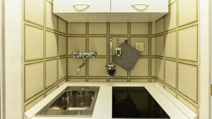 A kitchen with a stainless steel sink, a black stove, and a white cabinet above. - Spanish Steps Cozy Studio (Rome)
