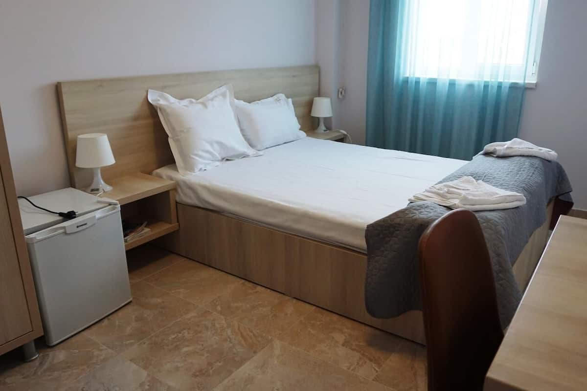 A neatly arranged hotel room with a bed, bedside tables, a small refrigerator, and a window with curtains.