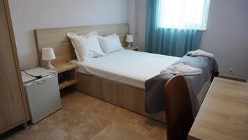 A neatly arranged hotel room with a bed, bedside tables, a small refrigerator, and a window with curtains.