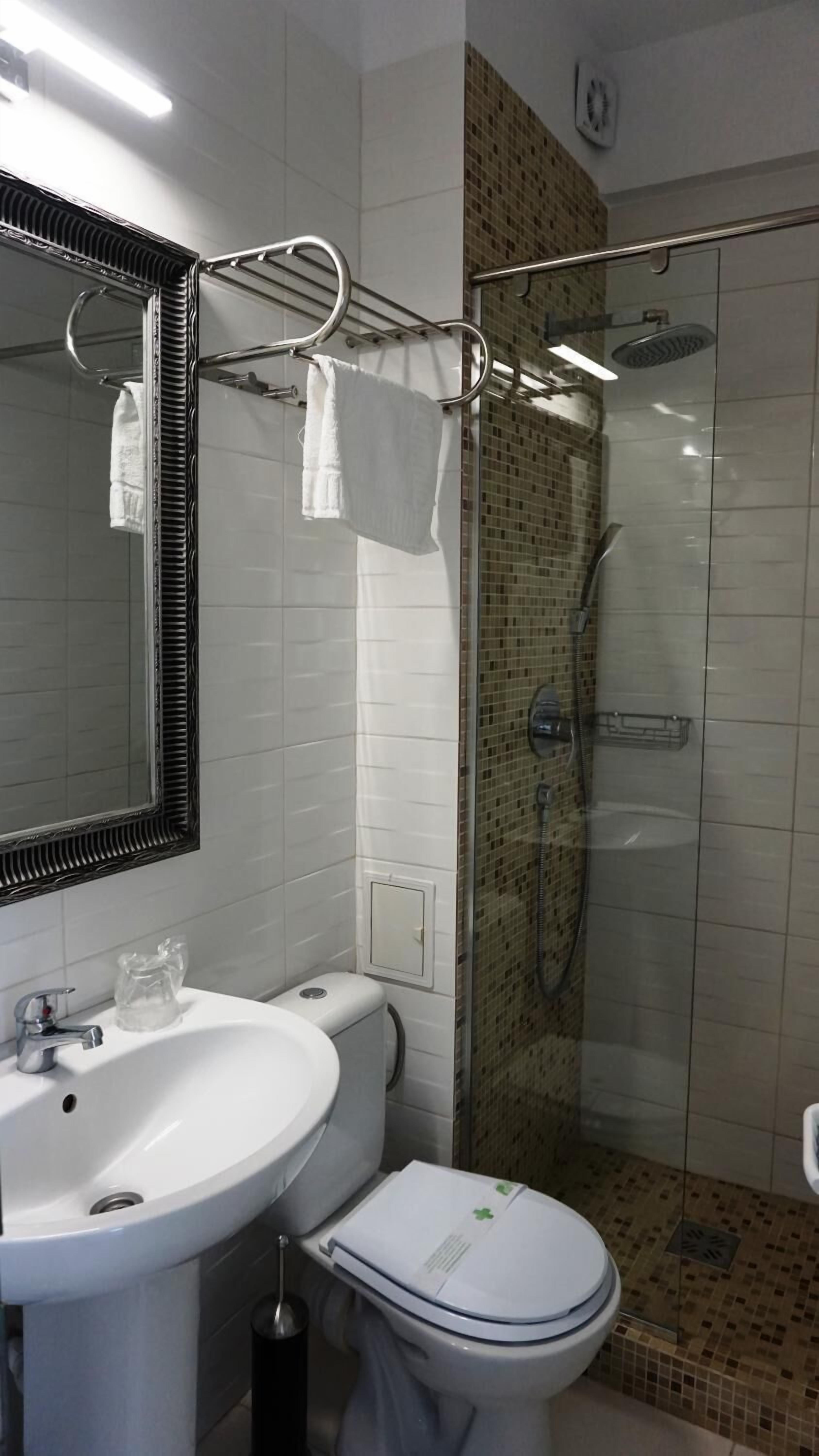 Ein Badezimmer mit Waschbecken in Weiß, Toilette, einer Duschkabine aus Glas und einem Spiegel mit schwarzem Rahmen.