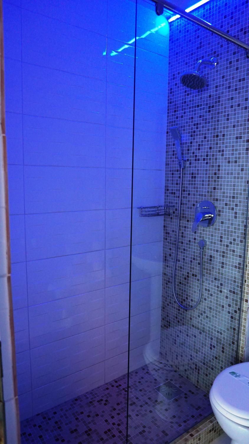 Zona de ducha con cerramiento de vidrio, pared con azulejos y ducha.