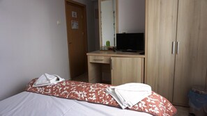 Un dormitorio con una cama, un escritorio de madera con televisor, un espejo y un armario.
