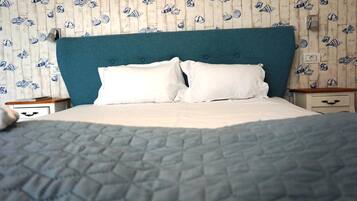 Una cama con cabecera color turquesa, ropa de cama blanca y un papel tapiz con motivos de peces.