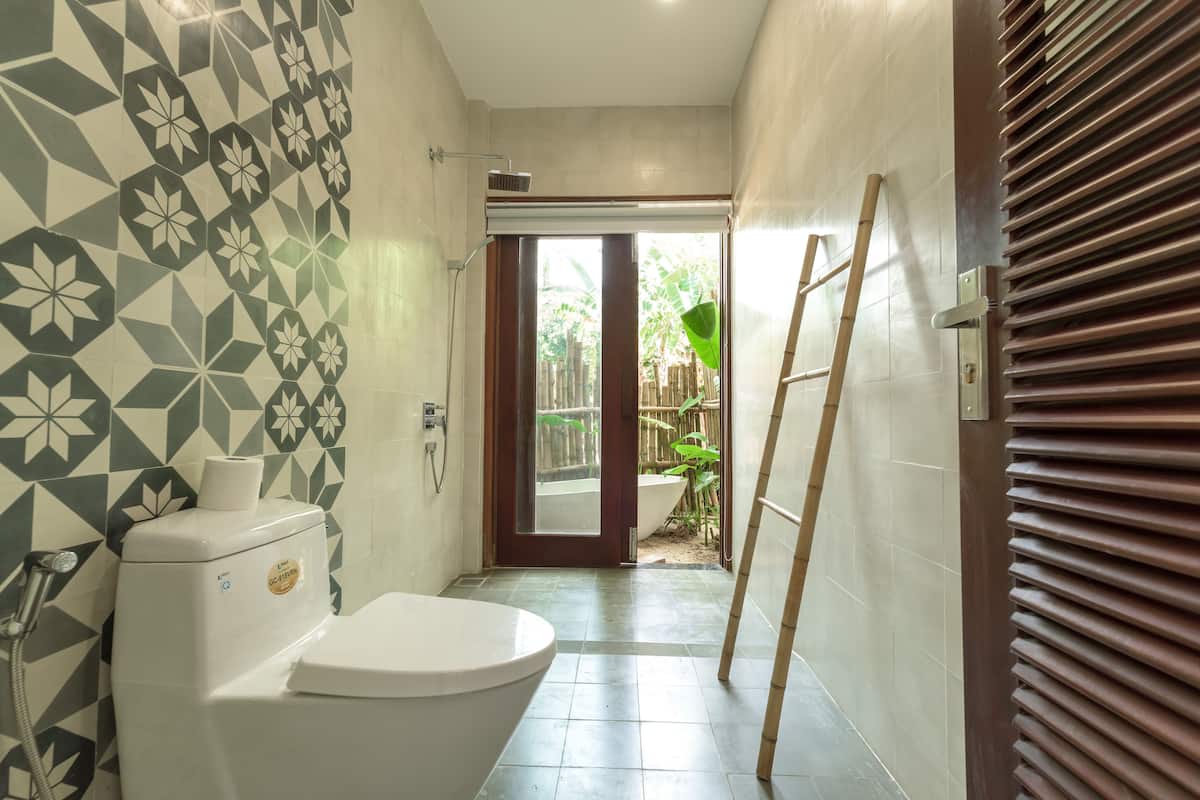 A bathroom with a toilet, a shower, and a window leading to a garden.