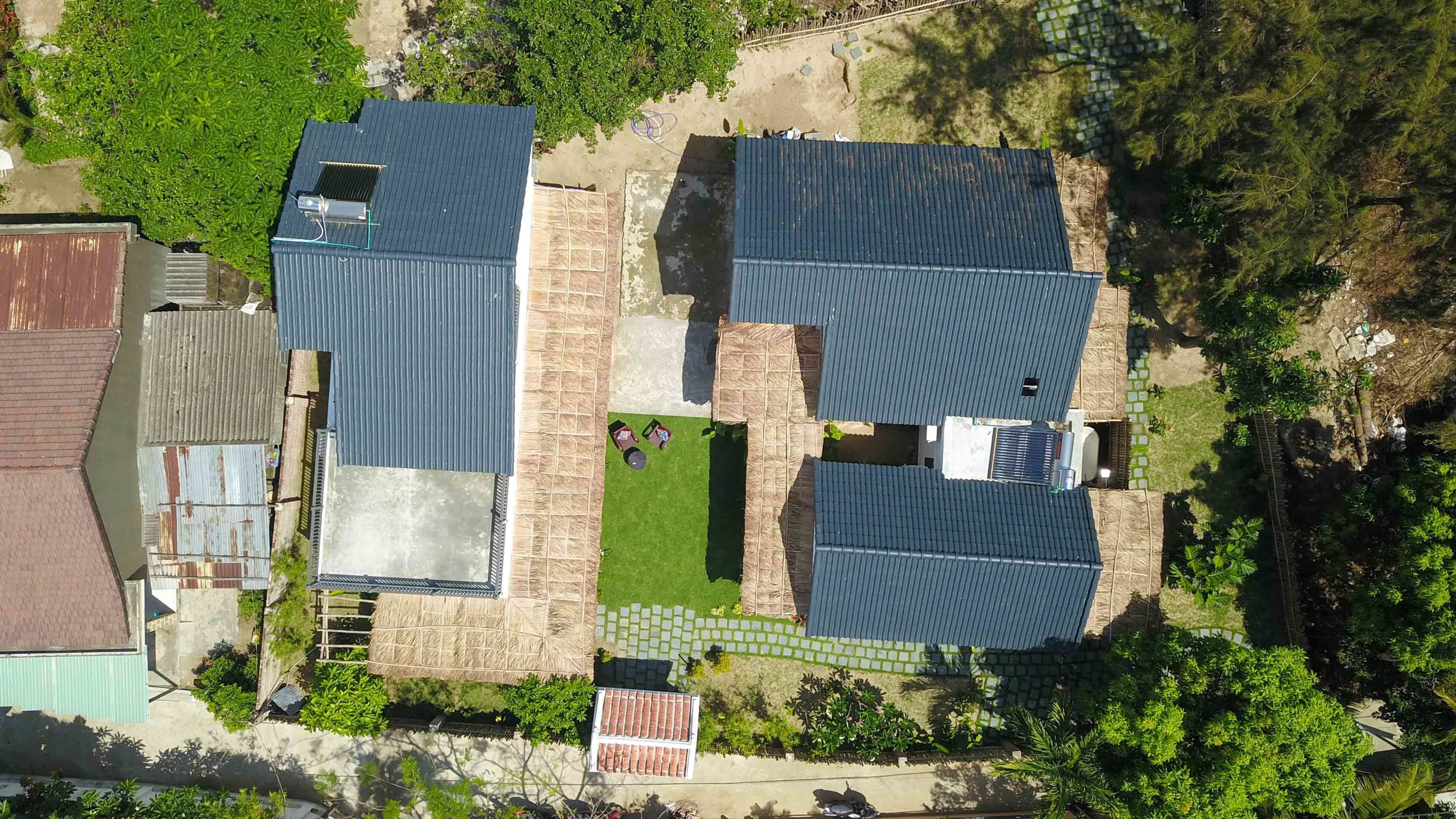 Vista aérea de una zona residencial con dos casas, cada una con techo azul, rodeadas de vegetación y un camino pavimentado.