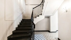Una escalera con barandillas negras que conduce a una plataforma. El piso tiene un diseño de baldosas geométricas.