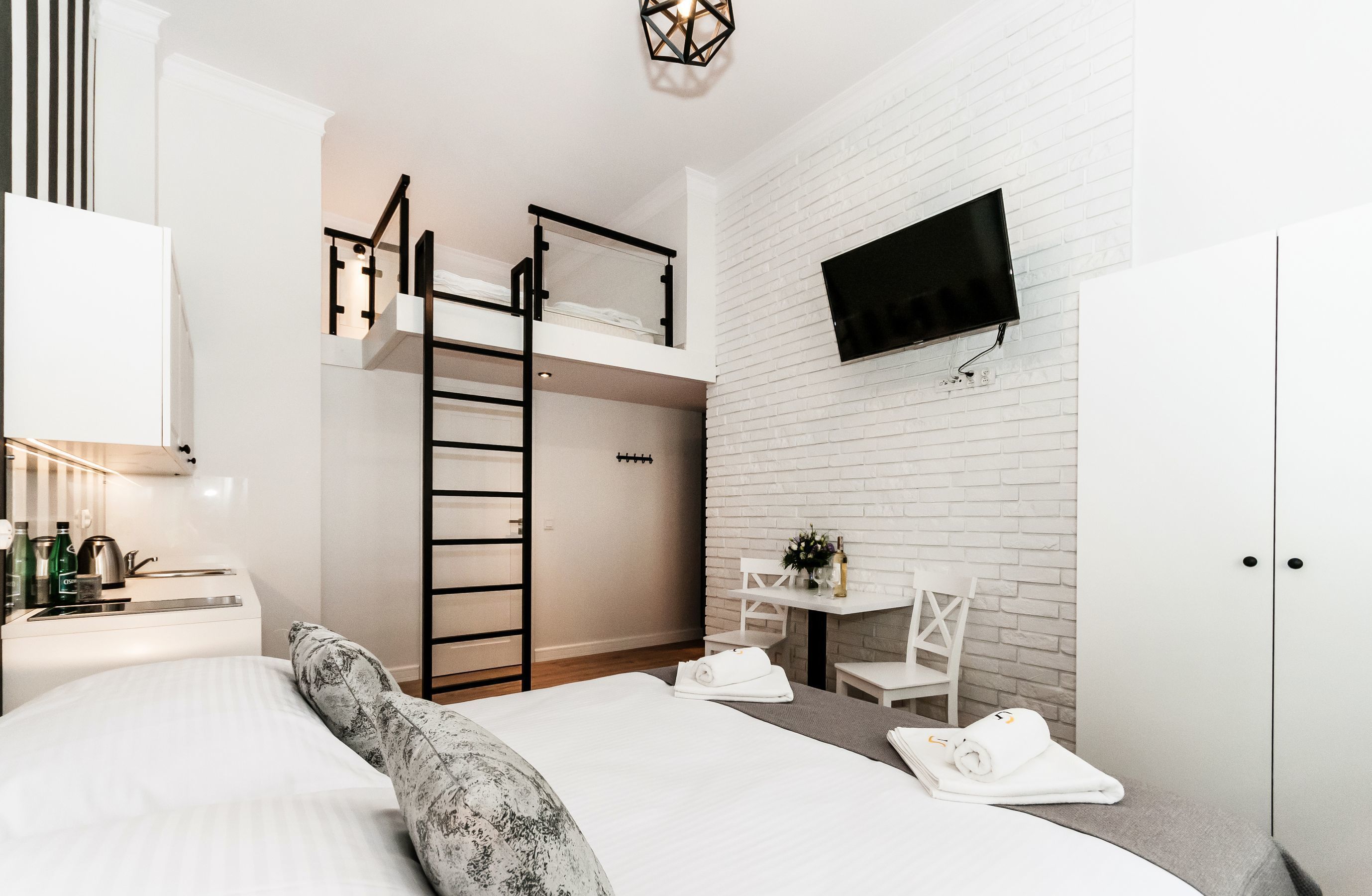 Une chambre d’hôtel moderne équipée d’un lit superposé, d’un bureau avec une chaise, d’un téléviseur fixé au mur et d’une armoire.