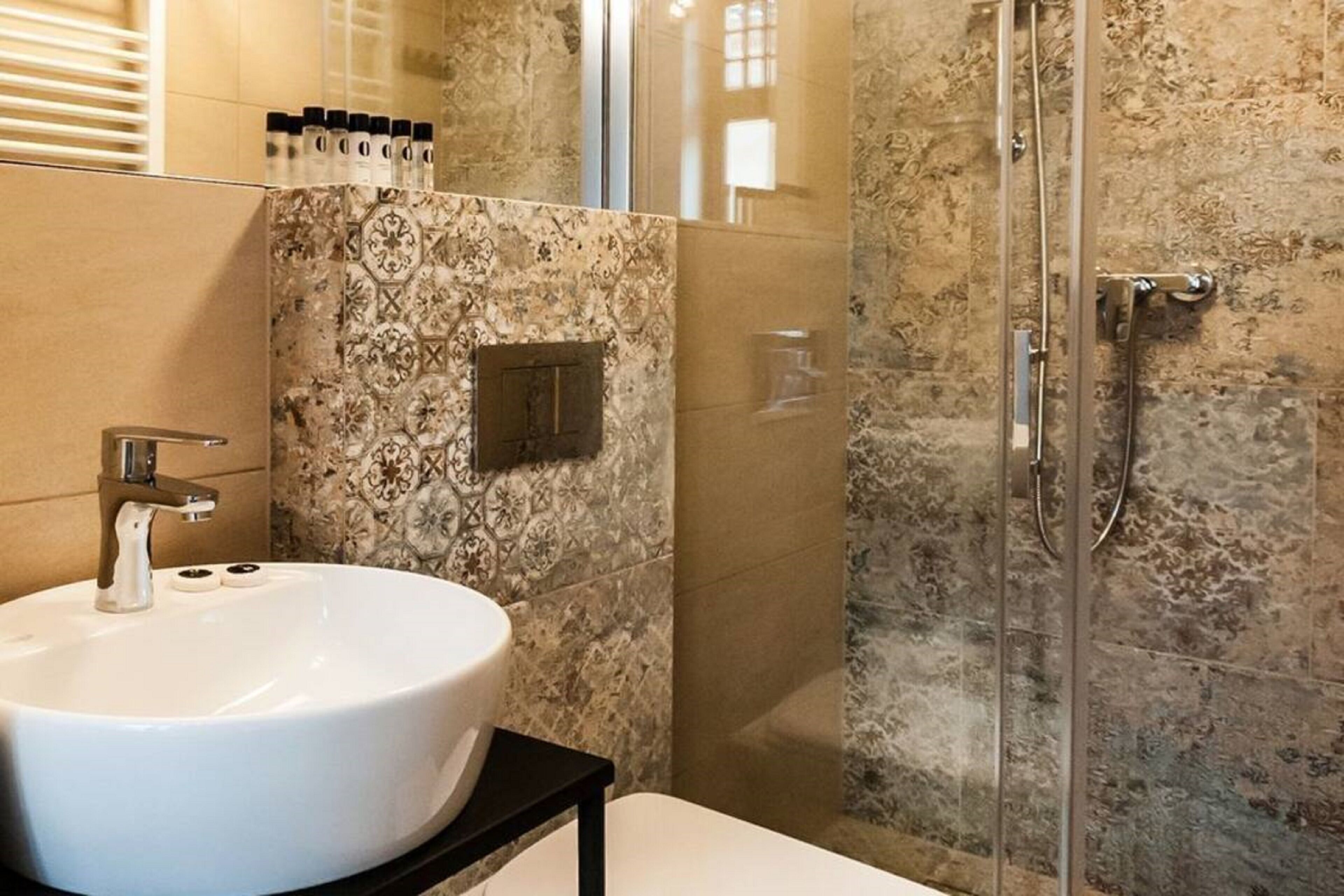 Une salle de bain avec un lavabo blanc, une cabine de douche en verre et des carreaux décorés.