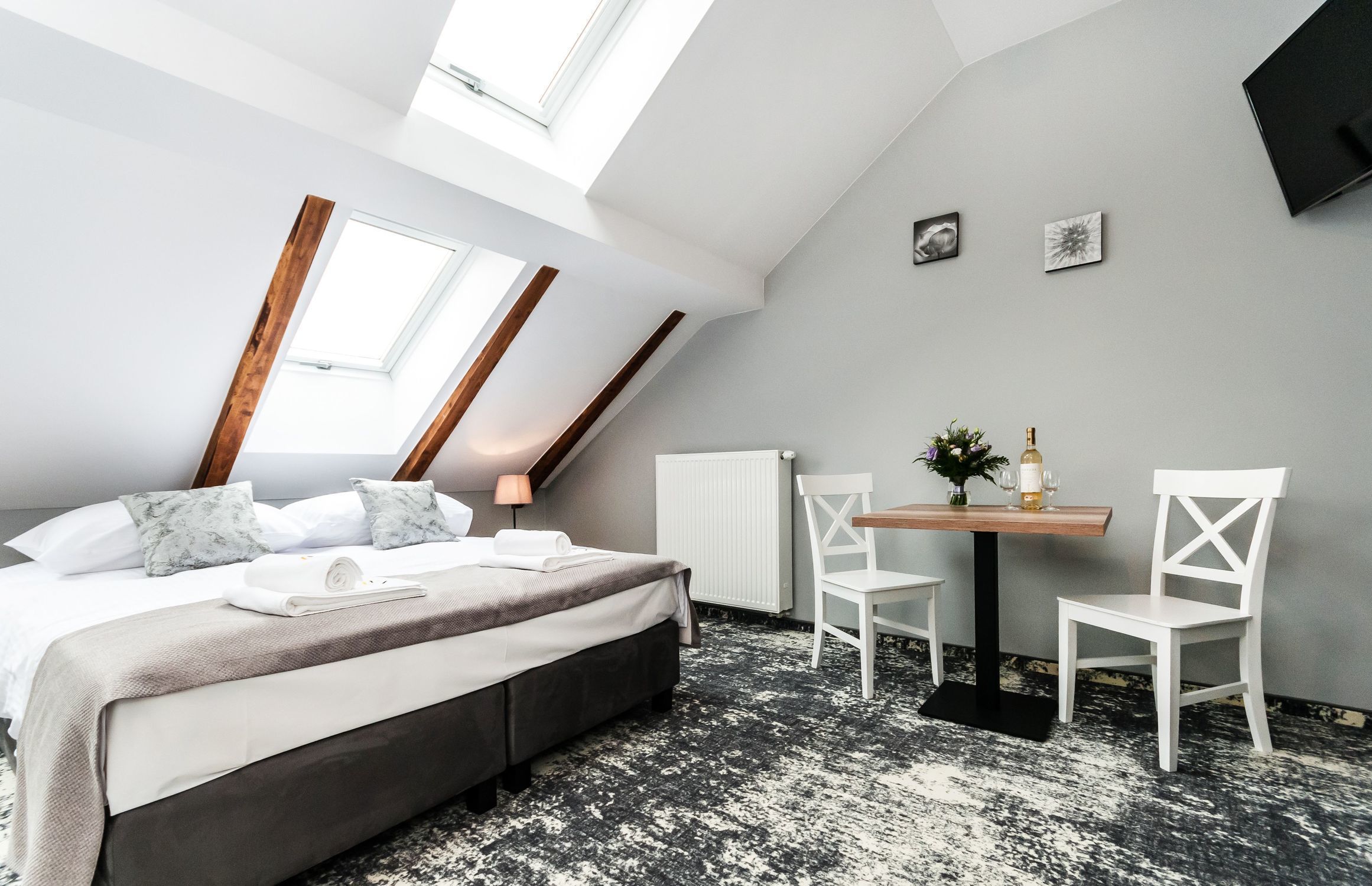 A modern bedroom with a skylight, a bed, a small table with chairs, and a radiator.