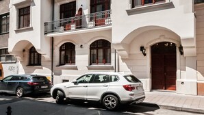 Un edificio de varios pisos con balcones, un coche estacionado al frente y un cielo despejado.