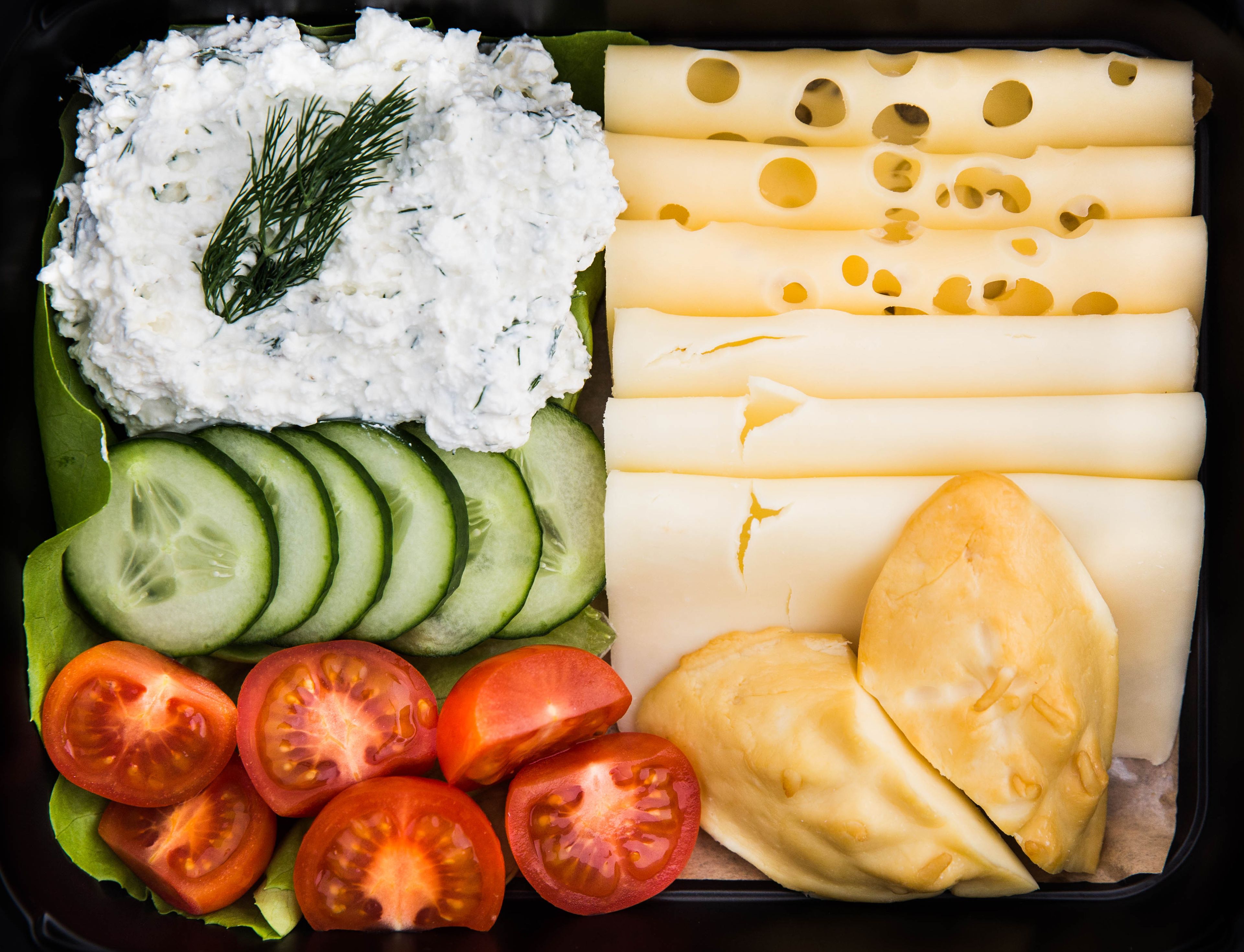 Uma refeição com queijo, pepino, tomate e um molho cremoso.