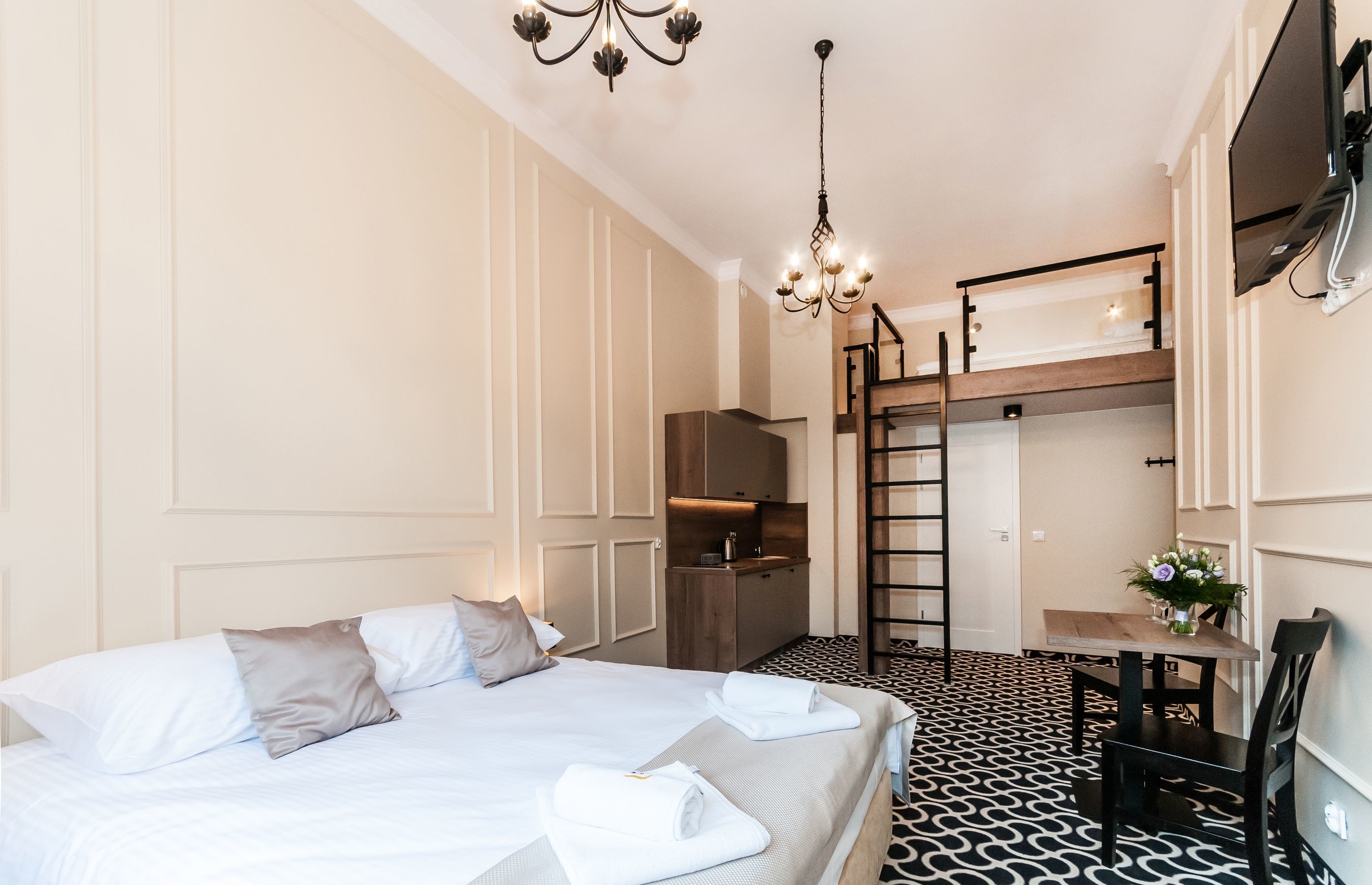 Habitación de hotel con cama, escritorio, silla, una mesita con un jarrón y una escalera que sube a un nivel superior.