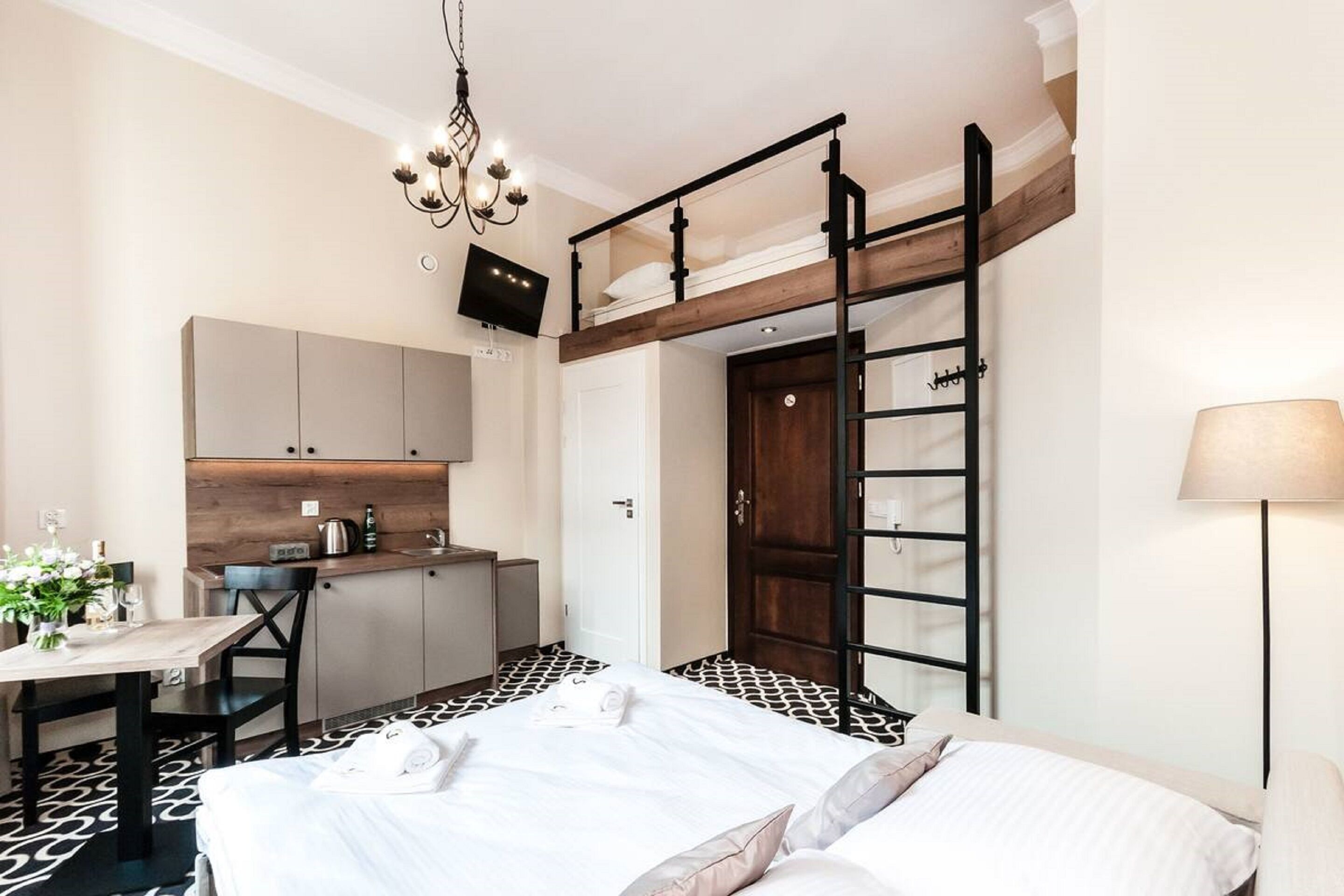A compact hotel room with a bunk bed, a kitchenette, a dining area, and a chandelier.