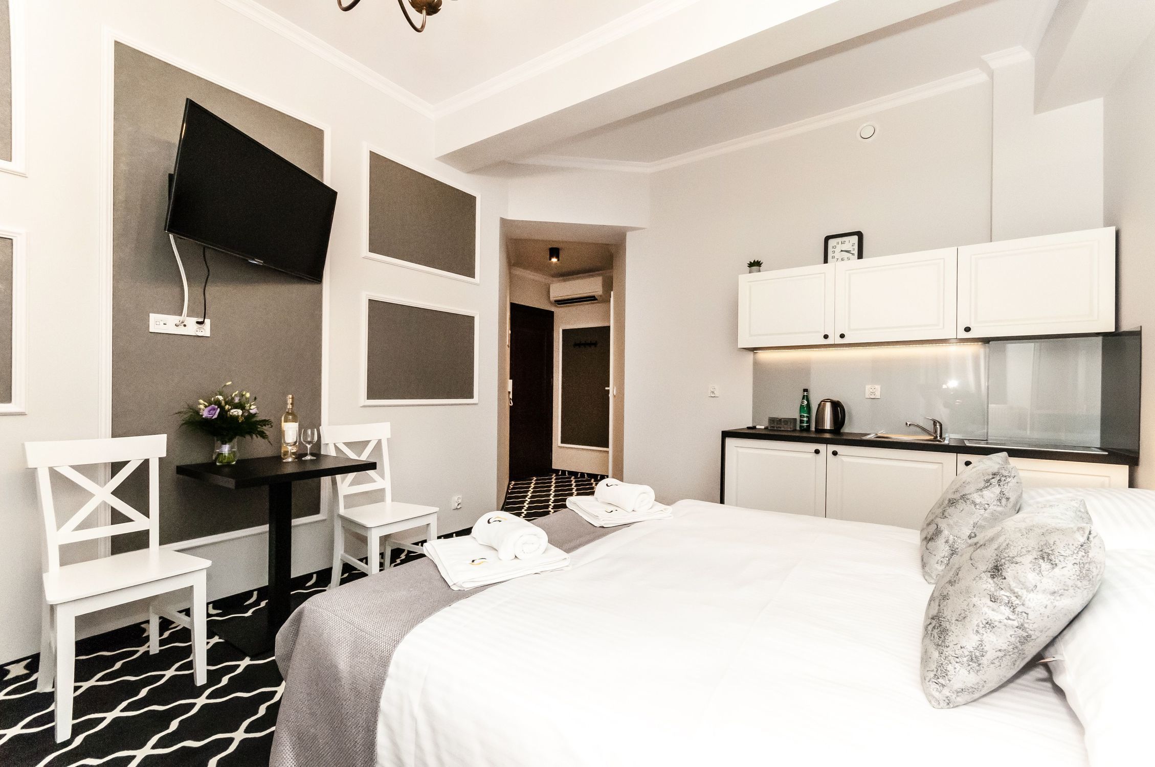 Ein Hotelzimmer mit Bett, Schreibtisch, Flachbildfernseher, einer kleinen Küche und einem durch eine offene Tür einsehbaren Badezimmer.