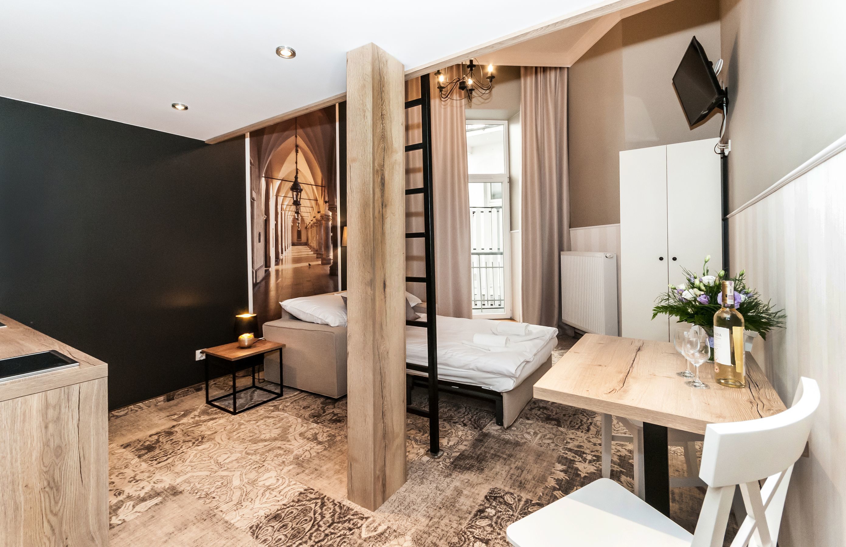 Ein modernes Schlafzimmer mit einem Bett, einem Schreibtisch und einem Stuhl. Eine Leiter führt zu einem Balkon, und ein Fernseher ist an der Wand befestigt.