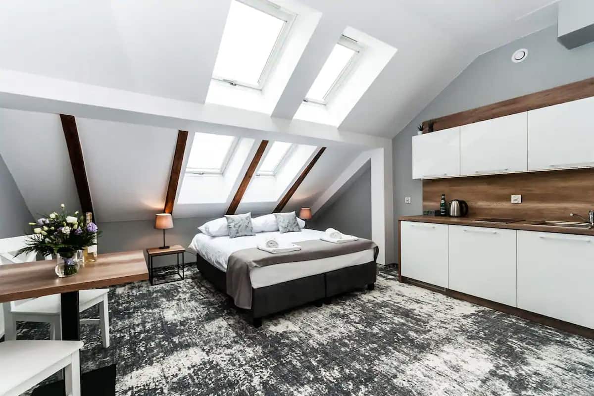 Quarto moderno estilo loft com claraboia, uma cama, escrivaninha e cozinha compacta.