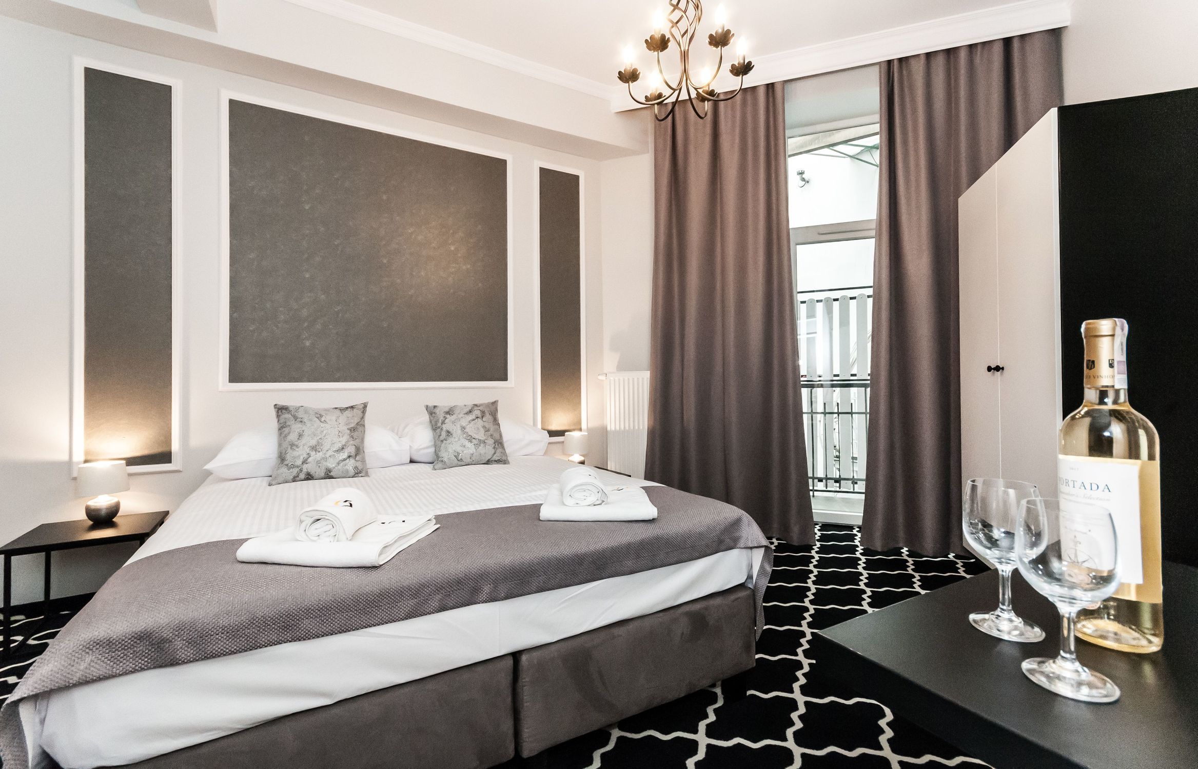 Ein Hotelzimmer mit einem großen Bett, zwei Nachttischen, einer Kristallleuchtre und Blick ins Freie.