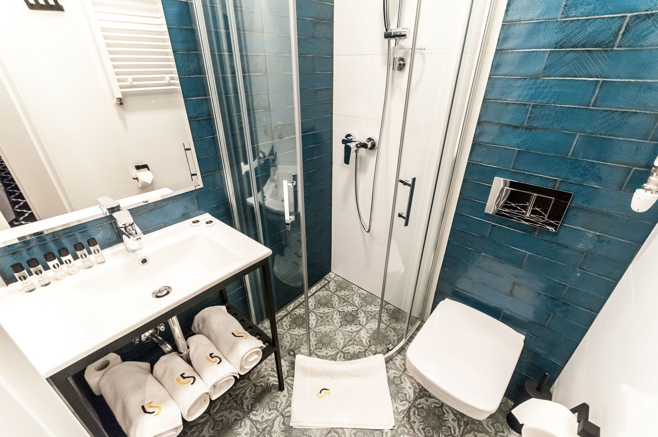 A bathroom with a glass-enclosed shower, a white sink with toiletries, and a toilet.