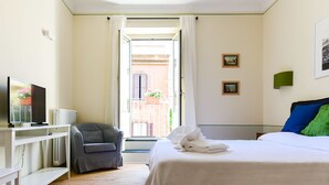 Ett hotellrum med en säng, en tv, en soffa och ett fönster med gardiner.