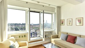 A spacious living room with a large window, a beige sofa, a wooden coffee table, and a city view. - Rome at Your Feet Apartment (Rome)