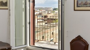 A room with a large window overlooking a cityscape, featuring a view of buildings and a distant tower. - Rome at Your Feet Apartment (Rome)