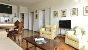 A living room with a wooden coffee table, two armchairs, a sofa, a TV, and framed floral artwork on the wall. - Rome at Your Feet Apartment (Rome)