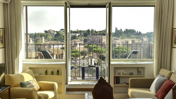 A room with a large window offering a view of a cityscape, including buildings and greenery. - Rome at Your Feet Apartment (Rome)