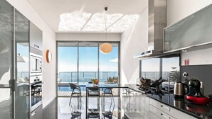 A modern kitchen with a glass dining area overlooking a pool and ocean.