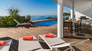 A poolside area with lounge chairs, a dining table, and a barbecue grill.