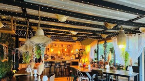 Ein gemütliches Restaurant mit Holztischen und -stühlen, Lichterketten und hängenden Pflanzen.