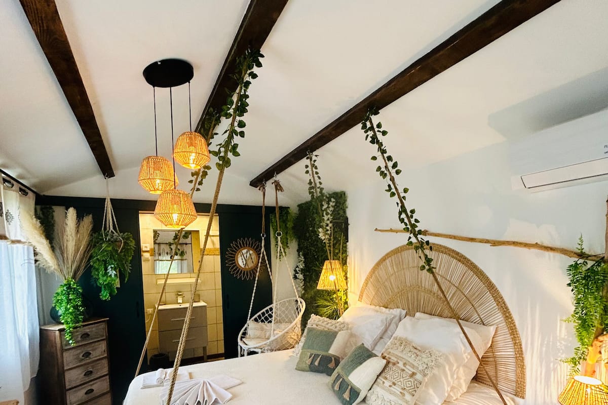 A bedroom with a large bed, hanging plants, and a wooden ceiling.