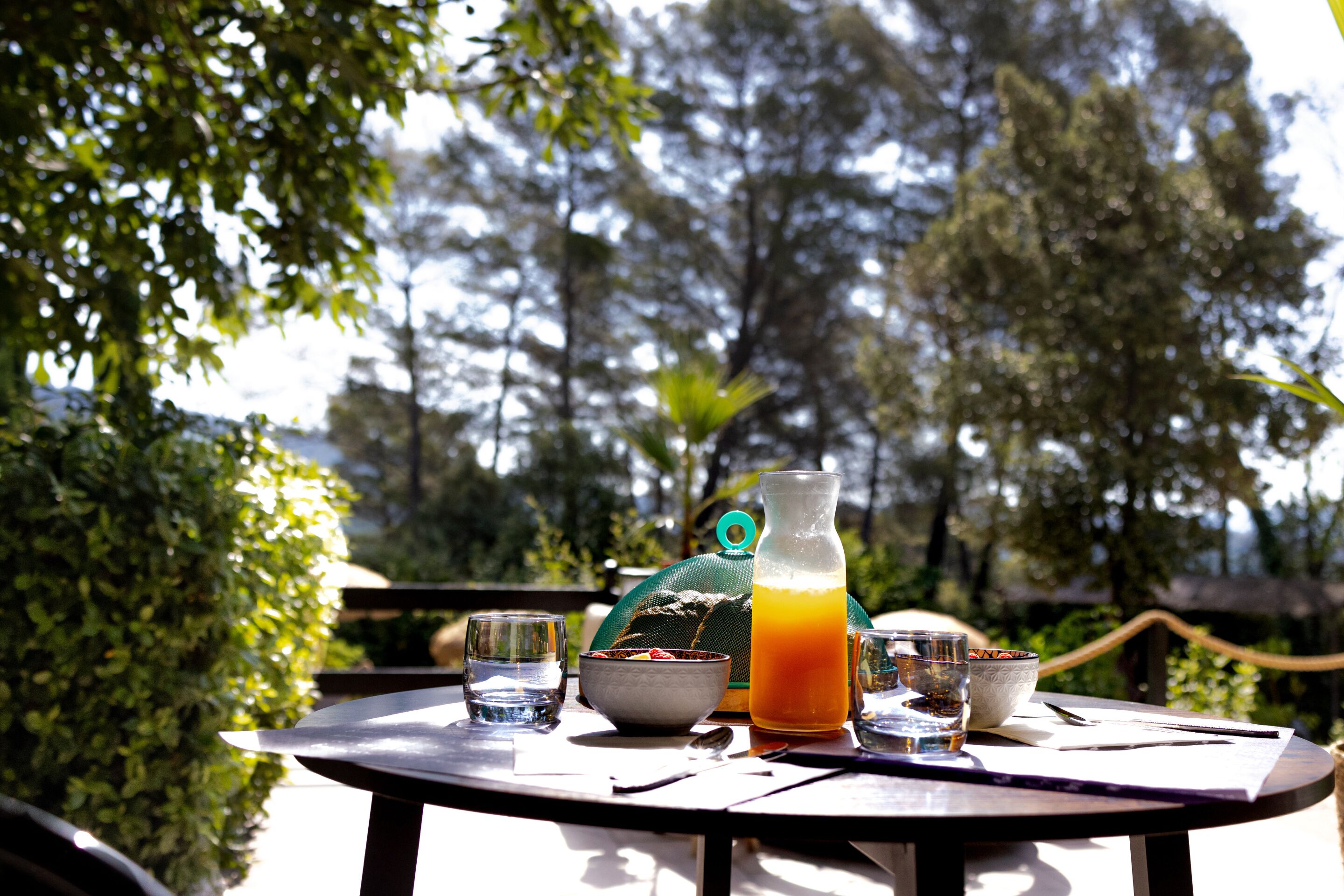 Une table ronde avec une carafe de jus d’orange, un bol, un verre et une cuillère.