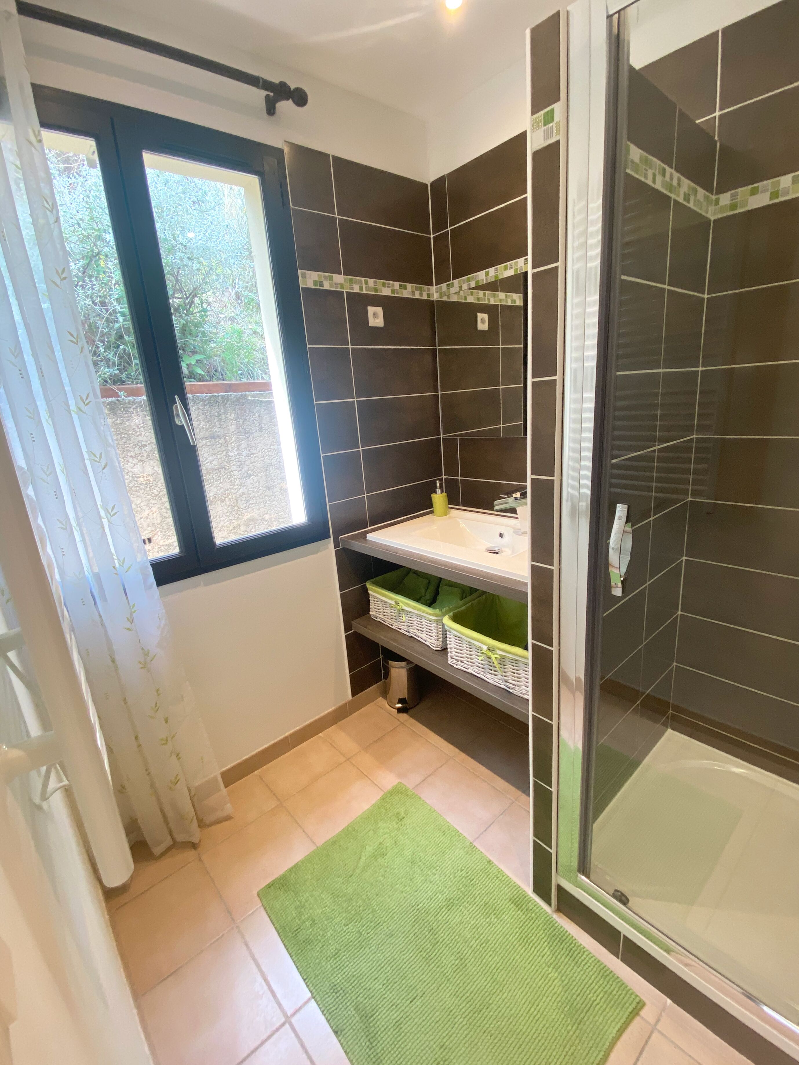 A bathroom with a shower, a window, and a sink.