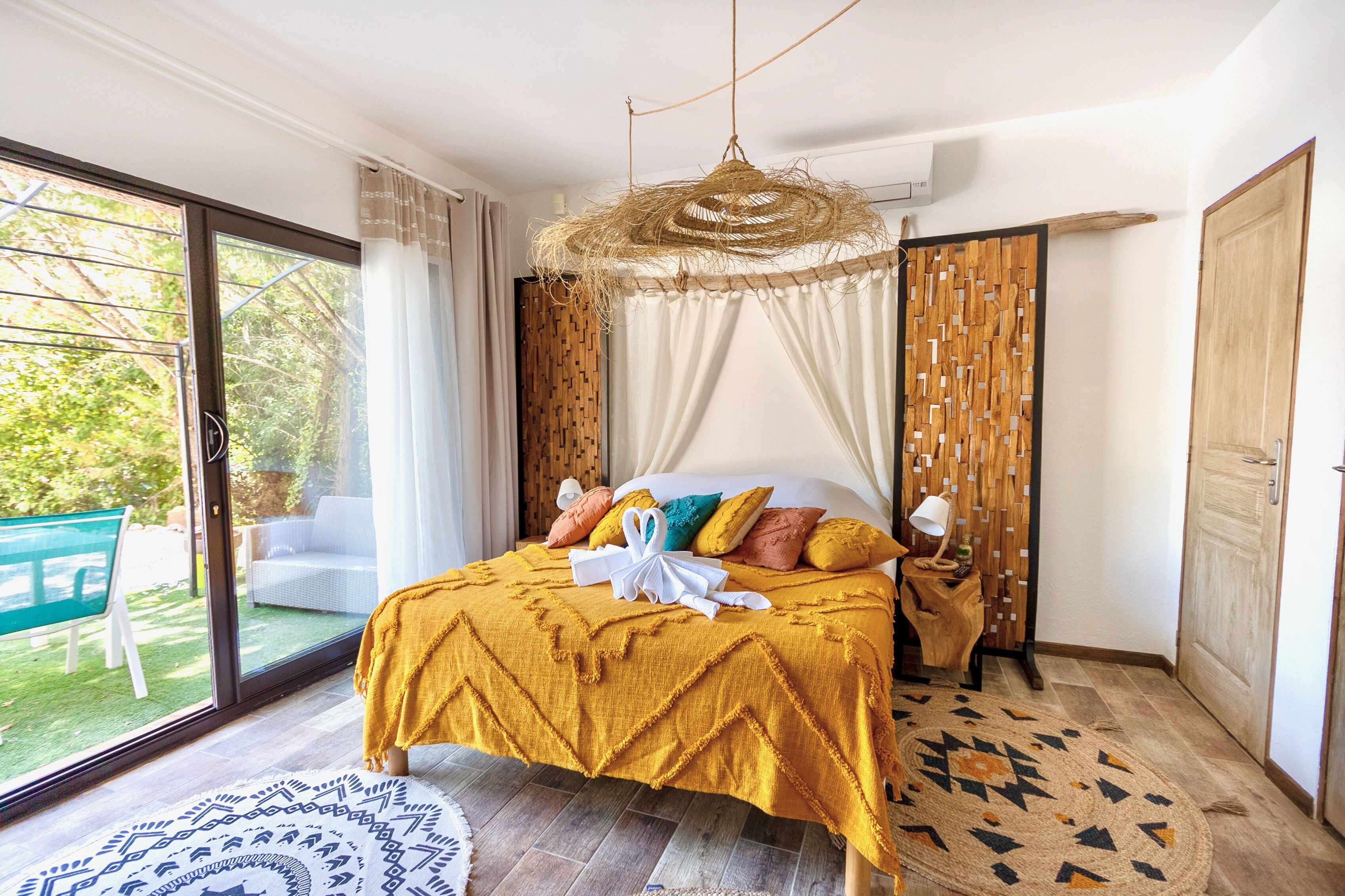 Een slaapkamer met een bed, nachtkastje, hanglamp en uitzicht op het groen.