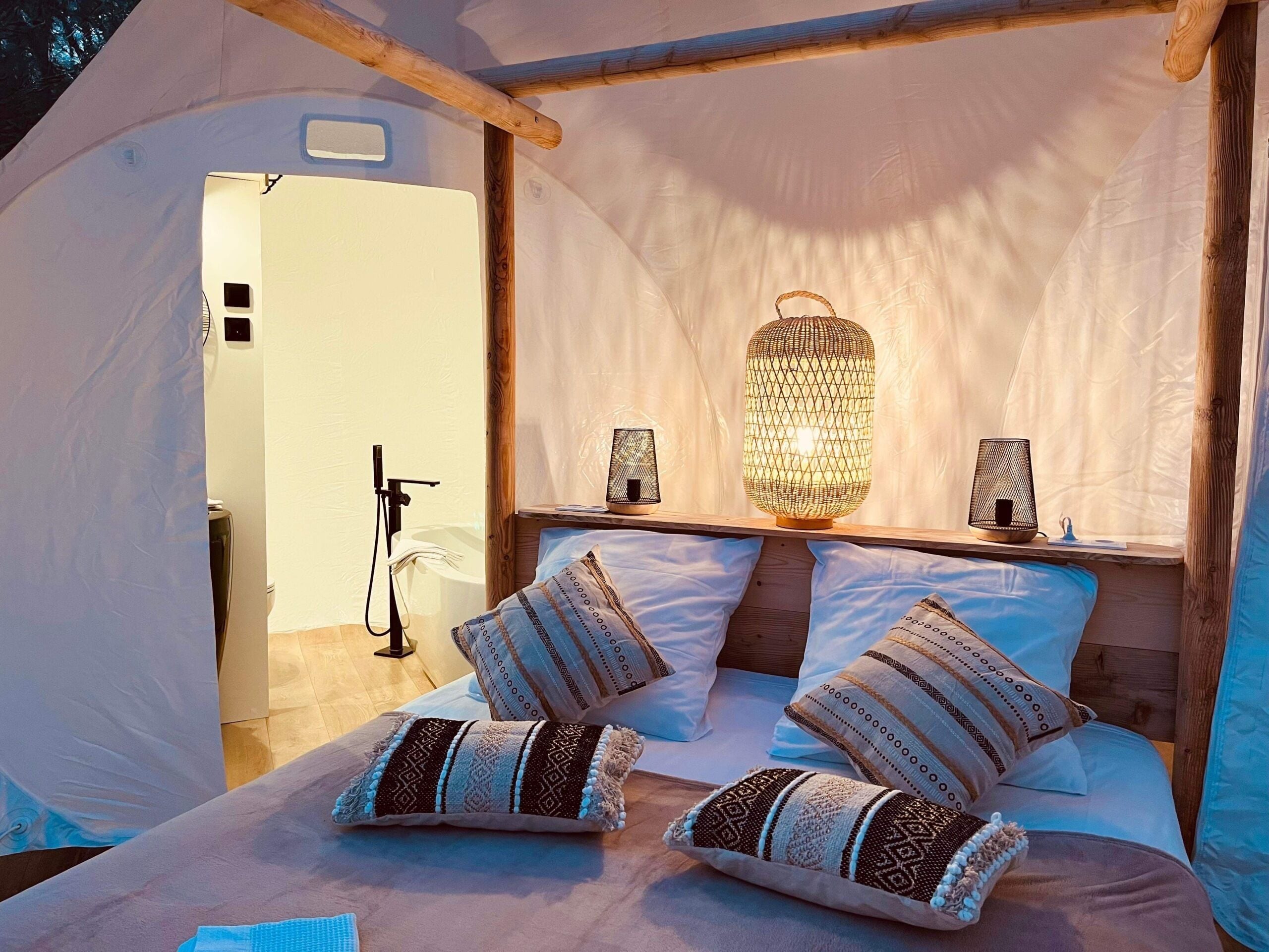 A cozy tent bedroom with a bed, patterned pillows, and two wall-mounted lamps.