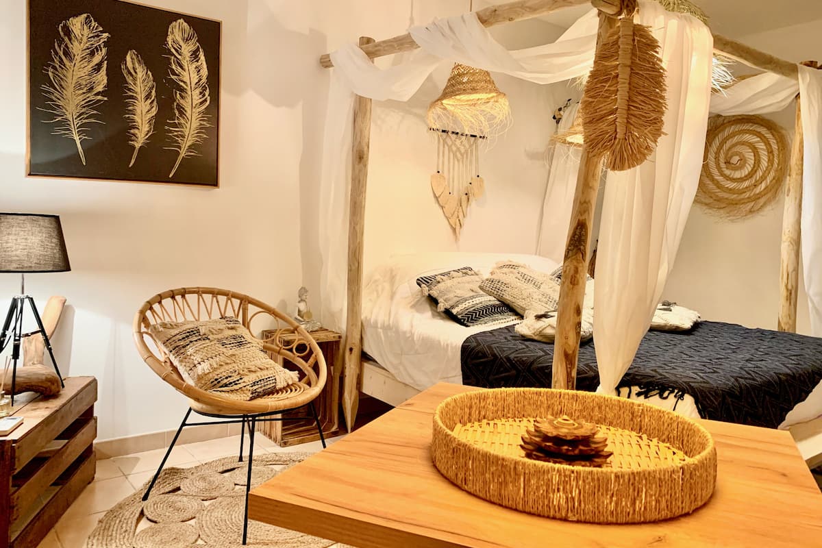 A room with a bed, a chair, a table, and a wall-mounted artwork.