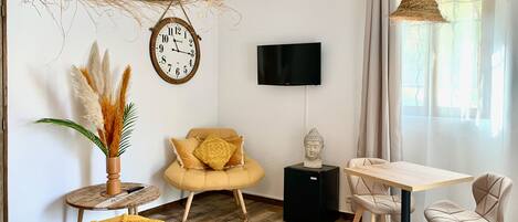 Una sala de estar moderna con un sofá amarillo, una mesita redonda pequeña, un televisor negro y un ventanal grande con cortinas.