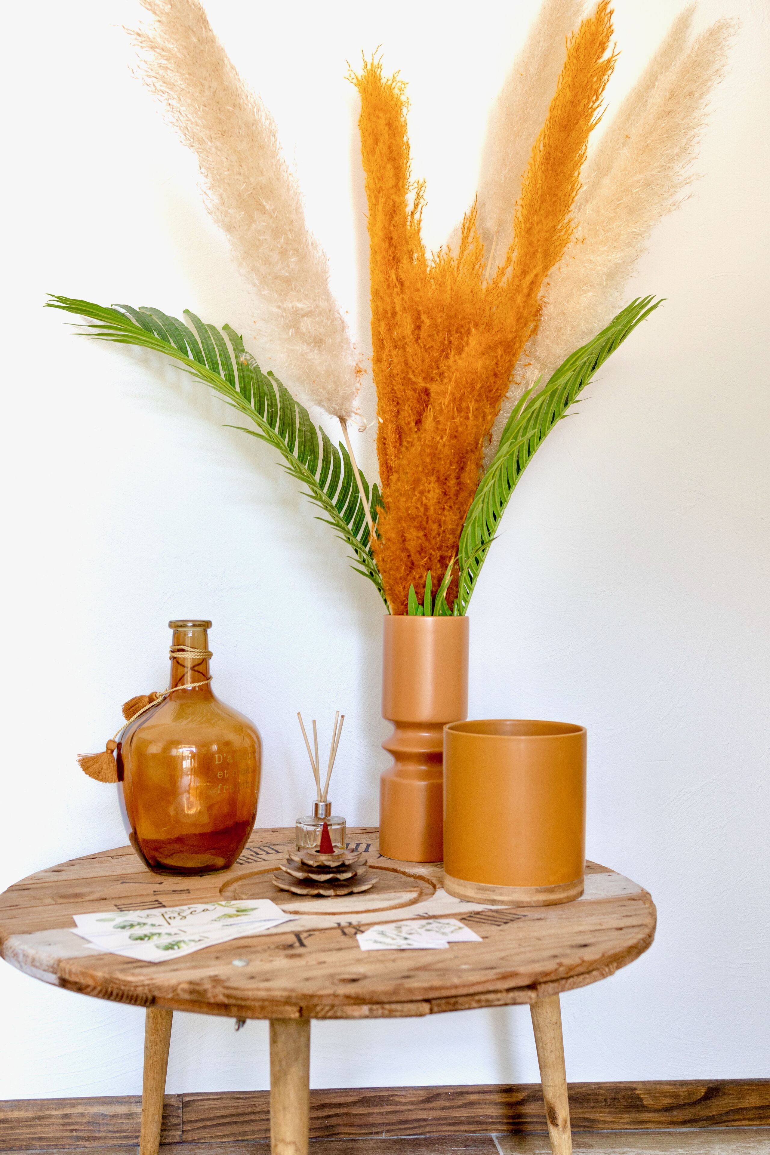 A round wooden table with a glass bottle, a candle, and a small decorative item.