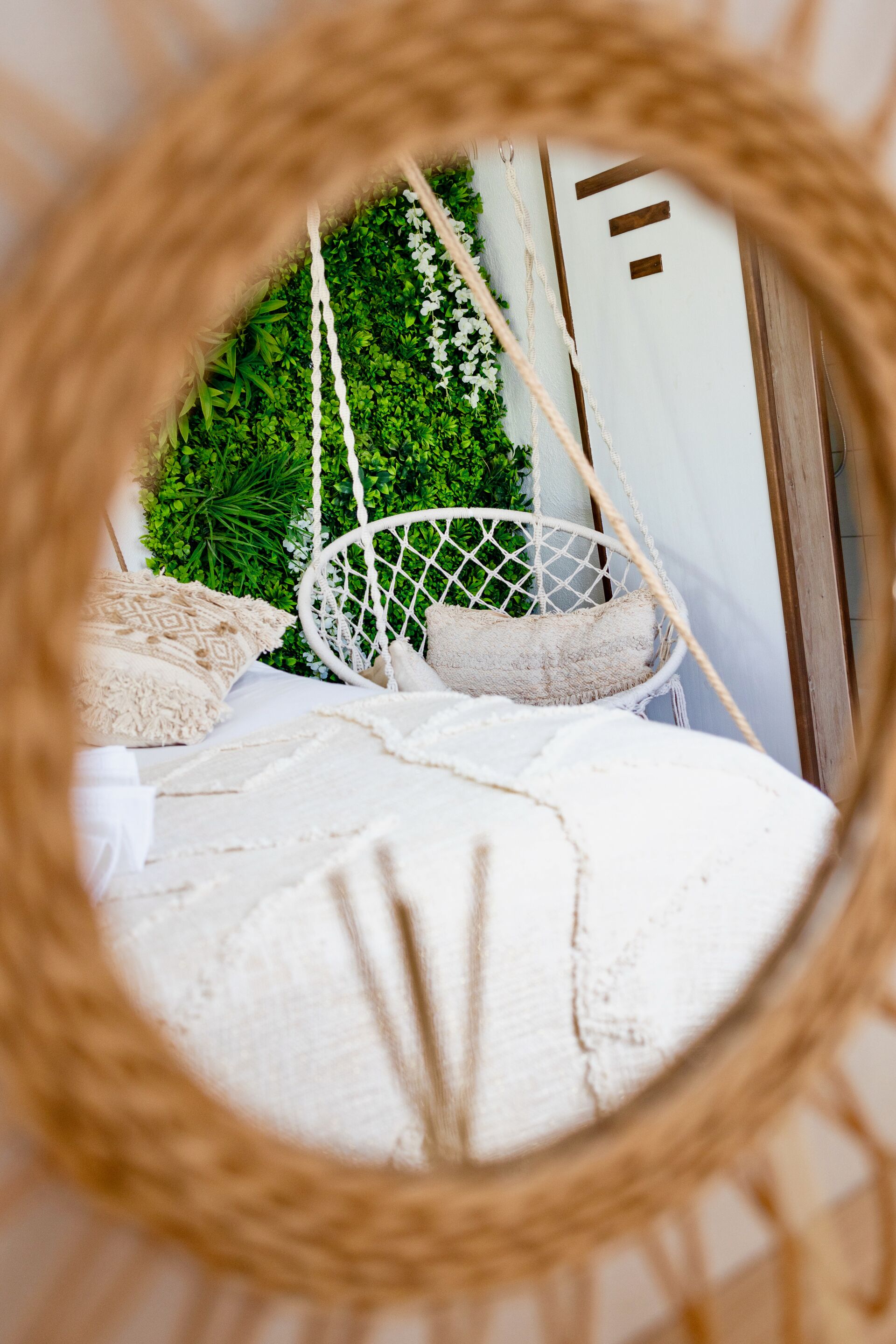 Una cama con colchón blanco y un sillón colgante con cuerdas.