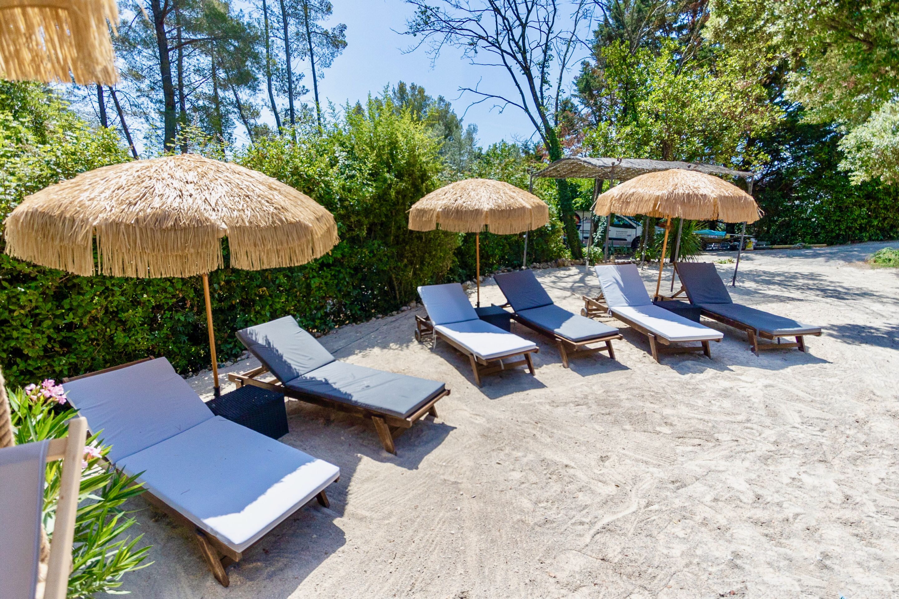 A beachside lounge area with wooden lounge chairs and thatched umbrellas, surrounded by greenery.