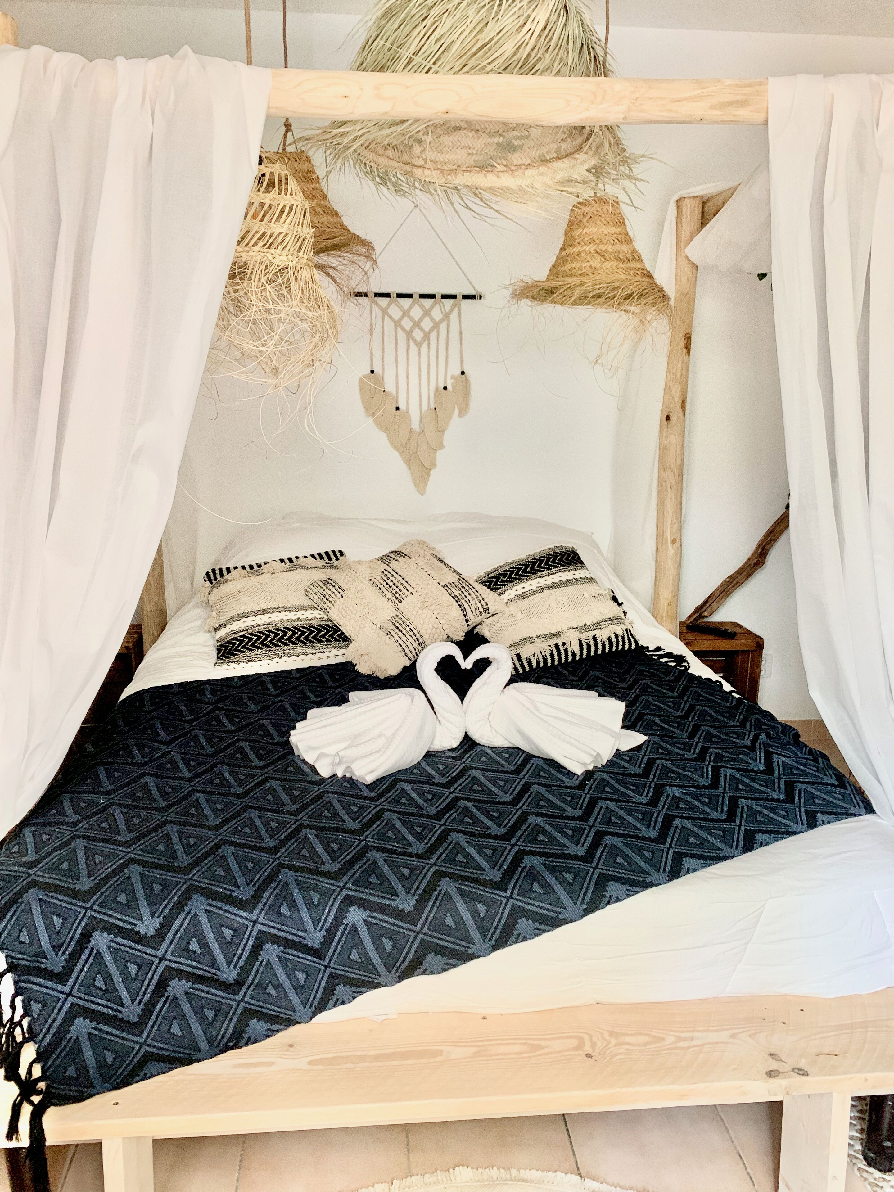 A bed with a geometric patterned blanket, two pillows with a heart design, and a dreamcatcher hanging above.