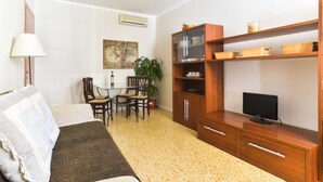 A living room with a sofa, a TV on a wooden stand, a dining table with chairs, and a potted plant. - Pantheon Cozy Apartment n. 4 (Rome)