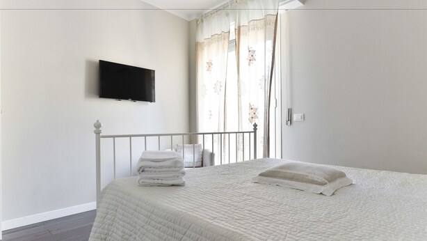 A bedroom with a bed, a TV mounted on the wall, and a window with curtains. - Pantheon Cozy Apartment n. 4 (Rome)