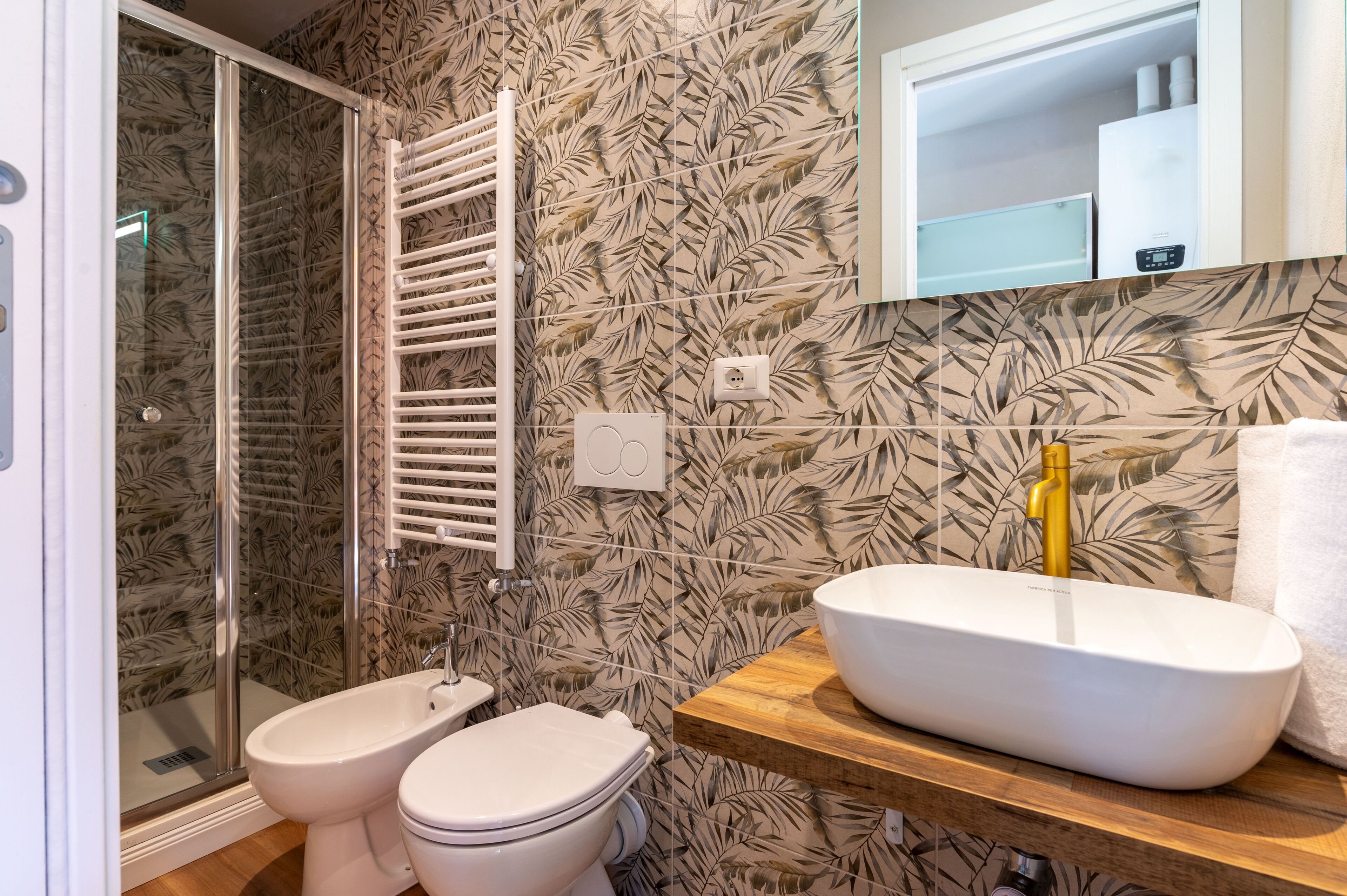 Un baño con ducha, inodoro y lavamanos, con un papel tapiz estampado con motivos de hojas.